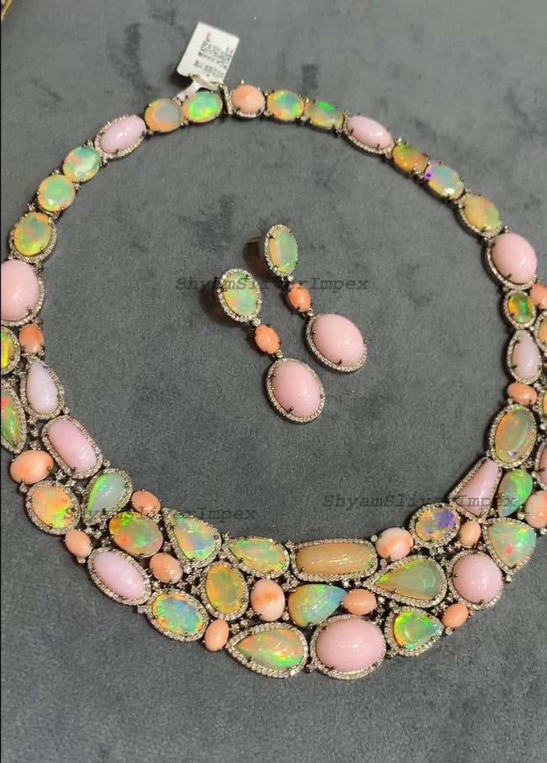 May include: A luxurious necklace and earring set featuring a variety of opal gemstones in shades of pink, yellow, and green. The jewelry is set in a silver metal with small, clear accent stones. The earrings have a drop design.