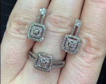 May include: A ring and matching earrings set. The jewelry features a square design with a central stone surrounded by smaller stones. The ring has a split band, and the earrings are drop style.