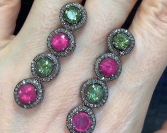 May include: A pair of dangle earrings with alternating pink and green gemstones set in silver. Each gemstone is surrounded by a halo of smaller diamonds.