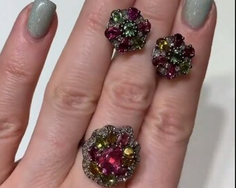 May include: A jewelry set consisting of a ring and two stud earrings. Each piece features a cluster of oval-cut pink, green, and yellow gemstones surrounded by small clear stones set in a dark metal frame with a floral-like arrangement.