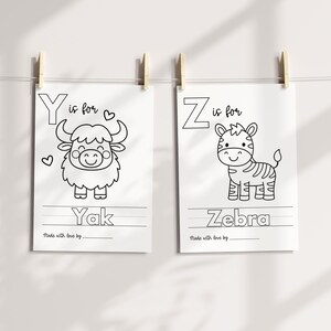 May include: Two black and white illustrated alphabet art prints. One features a yak with the text "Y is for Yak", and the other shows a zebra with the text "Z is for Zebra". Both prints are hanging with wooden clips.