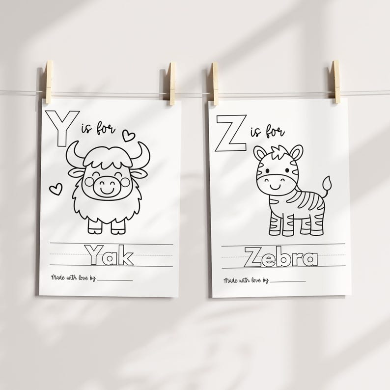 May include: Two black and white illustrated alphabet art prints. One features a yak with the text "Y is for Yak", and the other shows a zebra with the text "Z is for Zebra". Both prints are hanging with wooden clips.