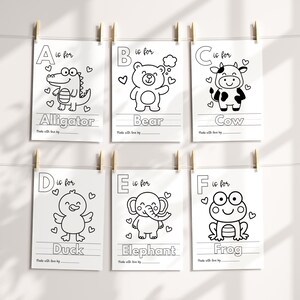 May include: Six white paper prints with black line drawings of animals and the alphabet. Each print features a different animal: alligator, bear, cow, duck, elephant, and frog. The prints are hanging from wooden clips.