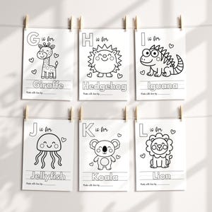 May include: Six white cards with black line drawings of animals, each with a letter and the animal's name: Giraffe, Hedgehog, Iguana, Jellyfish, Koala, and Lion. The cards are clipped to a string with wooden clothespins.