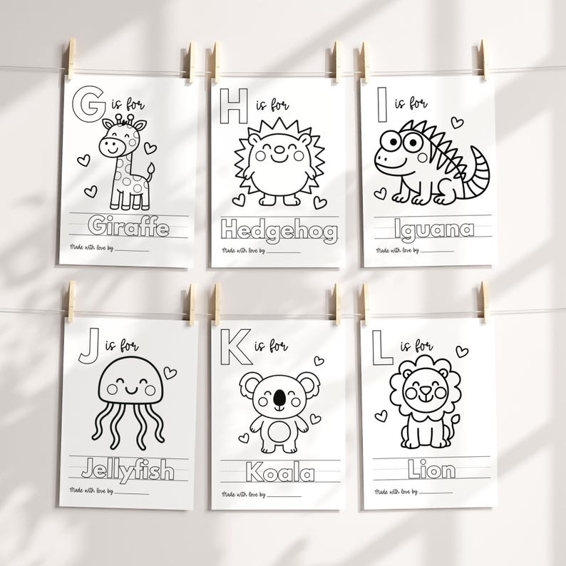 May include: Six white cards with black line drawings of animals, each with a letter and the animal's name: Giraffe, Hedgehog, Iguana, Jellyfish, Koala, and Lion. The cards are clipped to a string with wooden clothespins.