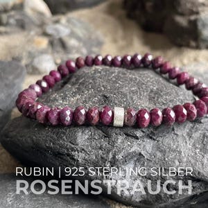 Könnte beinhalten: Ein Armband aus kleinen, facettierten, tiefroten Rubinperlen in kreisförmiger Anordnung. Eine einzelne, zylindrische, texturierte Silberperle ist zwischen den Rubinperlen platziert. Der Text RUBIN | 925 STERLING SILBER ROSENSTRAUCH ist sichtbar.