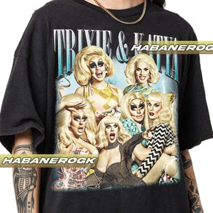 May include: Black t-shirt with a graphic print of six drag queens. The text "Trixie & Katya" is printed in white on the shirt. The queens are wearing colorful outfits and have dramatic makeup.