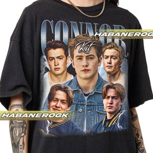 May include: Black t-shirt with a graphic print of four young men. The graphic features the text "Connor Kit" in a silver font. The men are wearing casual clothing and have a youthful appearance.