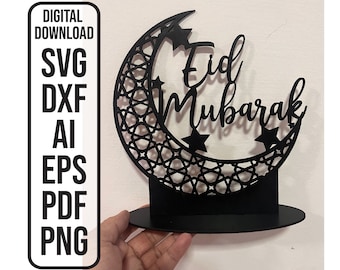 Può includere: Taglio nero di una luna crescente con un motivo geometrico e le parole "Eid Mubarak" in un carattere decorativo. La luna è su un supporto nero.