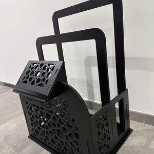 May include: Black wooden stand with intricate cutouts, featuring a shelf and two open compartments. The stand is designed to hold books or other items.