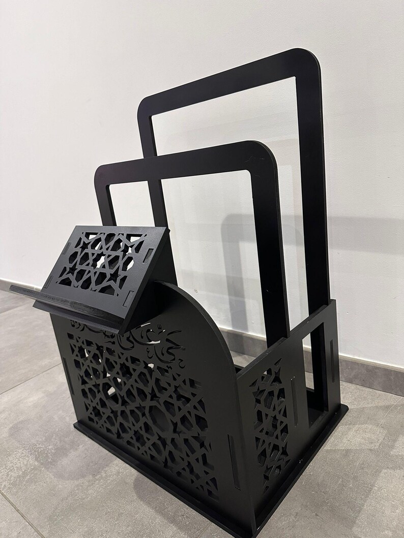 May include: Black wooden stand with intricate cutouts, featuring a shelf and two open compartments. The stand is designed to hold books or other items.