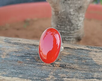 May include: A silver ring with a large, oval-shaped red gemstone. The ring is sitting on a wooden surface.