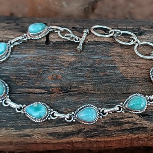Peut inclure: Un bracelet en argent avec un motif de pierres précieuses turquoise. Le bracelet a un fermoir à glissière et est fait de cercles liés.