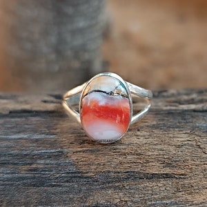 May include: A silver ring with an oval-shaped red, white, and brown gemstone. The ring has a simple design with a thin band.