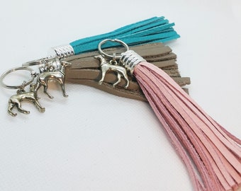Op de afbeelding: Een set van drie sleutelhangers met leren kwastjes in turquoise, bruin en roze. Elke sleutelhanger heeft een zilveren bedel in de vorm van een windhond.
