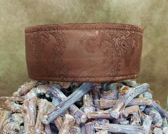 May include: A brown fabric collar with a paisley pattern. The collar is sitting on a pile of sticks.