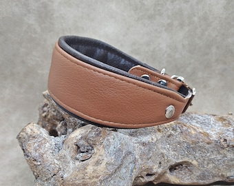 May include: A brown leather dog collar with a black interior and silver-tone hardware. The collar is wide and features a rounded design. The collar is displayed on a piece of driftwood against a neutral background.