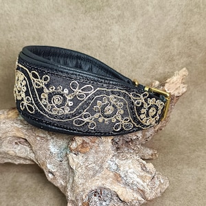 Könnte beinhalten: Schwarzes Lederhundekragen mit goldener Stickerei. Das Halsband hat ein dekoratives Muster aus Spiralen und Blumen.