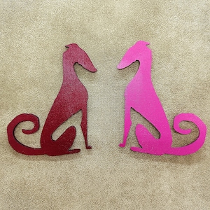 Könnte beinhalten: Zwei aus Holz ausgeschnittene Silhouetten von Windhunden, eine rot und eine rosa, die sich gegenüberstehen. Die Silhouetten sind schlicht und elegant.