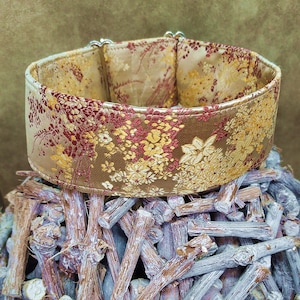 Könnte beinhalten: Ein gold- und rot gemustertes Hundehalsband mit einer silbernen Schnalle. Das Halsband ist aus einem weichen, luxuriösen Stoff gefertigt und perfekt für einen besonderen Anlass.