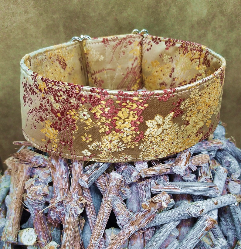 May include: A gold and red patterned dog collar with a silver buckle. The collar is made of a soft, luxurious fabric and is perfect for a special occasion.