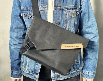 May include: A black crossbody bag made of washable kraft paper. The bag has a flap closure and a black adjustable strap. The bag has a brown label that says "Washable kraft paper".