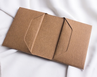 May include: A brown paper envelope with three folds. The envelope is open and the inside is visible. The text "FOLDD" is printed in black on a white background.