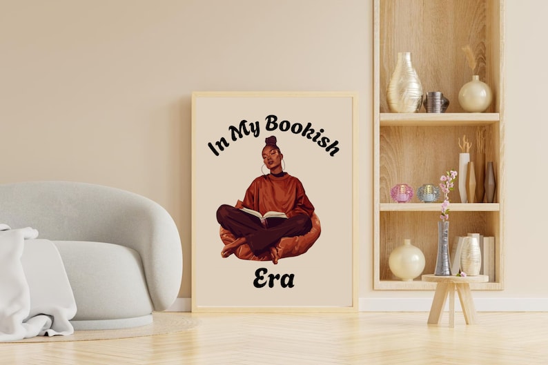 Op de afbeelding: Een ingelijst afdruk met een vrouw die op een stoel zit en een boek leest. De tekst op de afdruk luidt "In My Bookish Era".