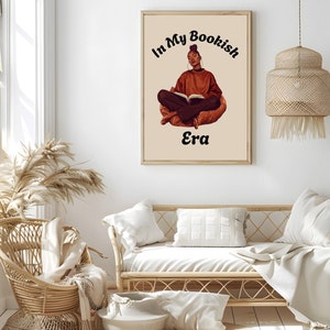 Op de afbeelding: Een digitale illustratie van een vrouw die in kleermakerszit zit en een boek leest. De tekst "In My Bookish Era" staat boven haar.
