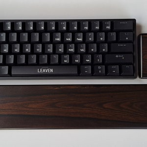 May include: A black keyboard with the word "LEAVEN" printed on the space bar. The keyboard is sitting on a dark brown wooden wrist rest and a smaller dark brown wooden wrist rest.