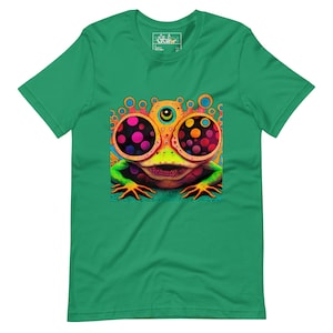 May include: Green t-shirt featuring a vibrant, psychedelic frog illustration. The frog has large, colorful eyes with polka dots, a third eye, and a wide grin. The design is centered on the shirt, creating a bold and eye-catching look.