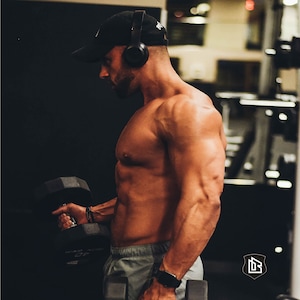 Peut inclure: Un homme torse nu portant un casque et une casquette de baseball noire soulève une haltère dans une salle de sport. Il porte un short de sport gris et une montre noire.