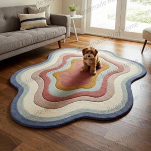 Può includere: Un tappeto astratto a forma di nuvola multicolore con un piccolo cane marrone seduto al centro. Il tappeto ha sfumature di blu, rosa, giallo e bianco.
