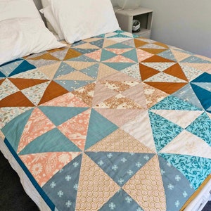 May include: A quilt with a geometric pattern in shades of teal, brown, and cream. The quilt is made of various fabrics with different patterns and textures.