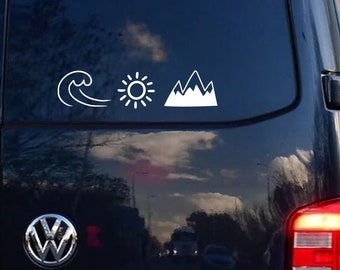 Op de afbeelding: Een zwarte bestelwagen met een witte golf, zon en berg sticker op de achterruit.
