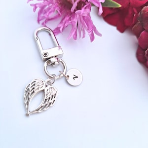以下が含まれることがあります： 天使の羽のチャームと数字の1が刻まれた小さな丸いタグが付いた、シルバーカラーのキーホルダー。 キーホルダーにはロブスタークラスプが付いています。 背景にはピンクと赤の花があります。