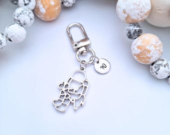May include: Silver-colored keychain featuring an astronaut charm with heart details. The keychain includes a round tag with the letter "W" and a clasp for attaching to keys or bags. Decorative beads surround the keychain.