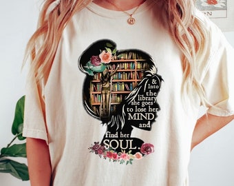 May include: A white t-shirt with a black silhouette of a woman standing in front of a bookshelf. The text reads "& Into the library she goes to lose her MIND and find her SOUL."
