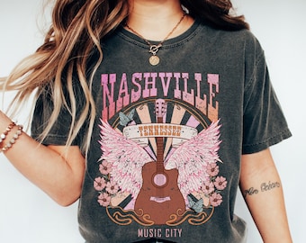 May include: A dark gray t-shirt with a vintage-style graphic of a guitar with wings and the text "Nashville Tennessee Music City".