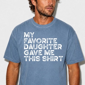 Pu&ograve; includere: T-shirt blu jeans con la scritta "MY FAVORITE DAUGHTER GAVE ME THIS SHIRT" in lettere bianche. La maglietta &egrave; a girocollo e ha maniche corte.