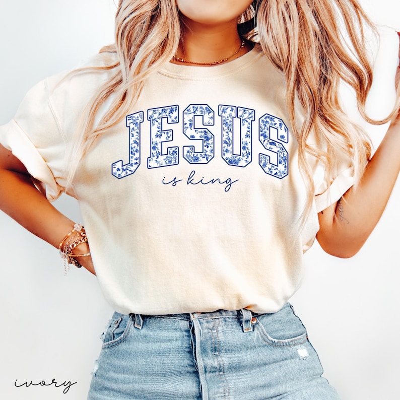 May include: A white t-shirt with a blue floral design that says "JESUS is king" in a vintage collegiate font.