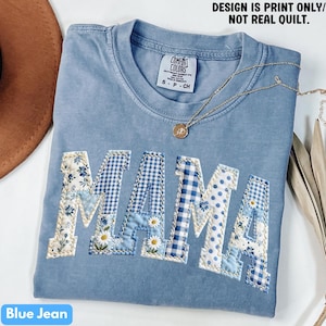May include: A blue jean colored t-shirt with the word "MAMA" in patchwork letters. The letters are decorated with floral, gingham, and polka dot patterns. The shirt has a crew neck and short sleeves. The text "DESIGN IS PRINT ONLY/ NOT REAL QUILT" is printed at the top.