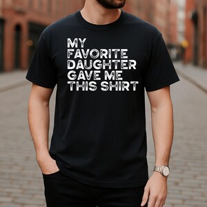 Pu&ograve; includere: T-shirt nero girocollo con la scritta bianca "MY FAVORITE DAUGHTER GAVE ME THIS SHIRT". La maglietta &egrave; realizzata in un materiale morbido ed &egrave; adatta per l'abbigliamento casual.