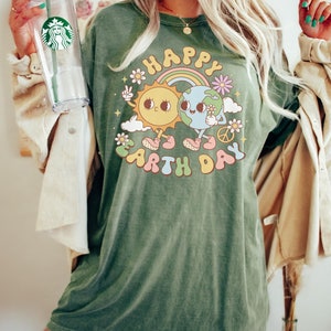 May include: A green t-shirt with a graphic of a smiling sun and earth holding hands. The graphic is surrounded by flowers and the text "Happy Earth Day".