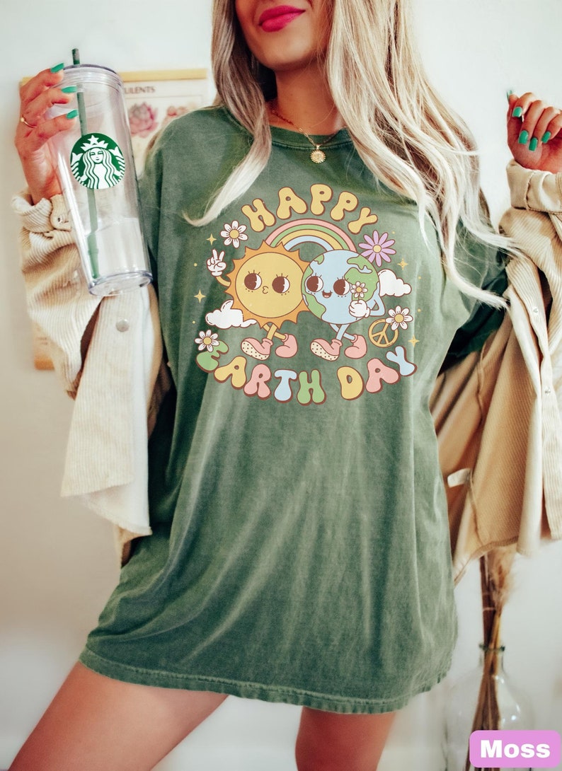 May include: A green t-shirt with a graphic of a smiling sun and earth holding hands. The graphic is surrounded by flowers and the text "Happy Earth Day".