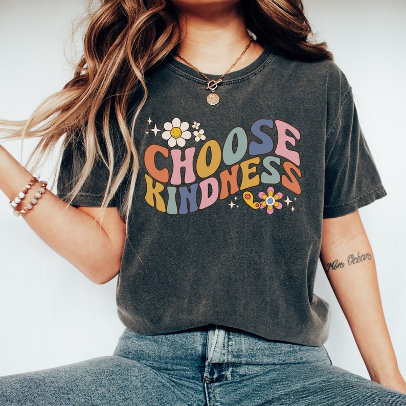 May include: A dark grey t-shirt with a retro-style graphic that says "Choose Kindness" in rainbow colours with flowers and stars.