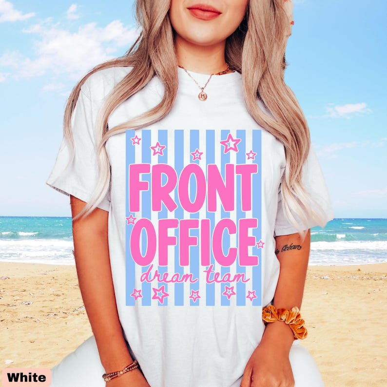 K&ouml;nnte beinhalten: Ein wei&szlig;es kurz&auml;rmeliges T-Shirt mit einem Grafikdruck aus hellblauen vertikalen Streifen. Der Text FRONT OFFICE ist in gro&szlig;en rosa Buchstaben gedruckt, darunter stehen die Worte dream team in rosa Schreibschrift, umgeben von kleinen rosa Sternen.