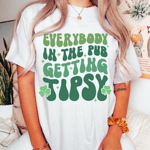 Puede incluir: Camiseta blanca con la frase "EVERYBODY IN THE PUB GETTING TIPSY" en verde. El dise&ntilde;o incluye tr&eacute;boles y estrellas. Un estilo casual y c&oacute;modo.
