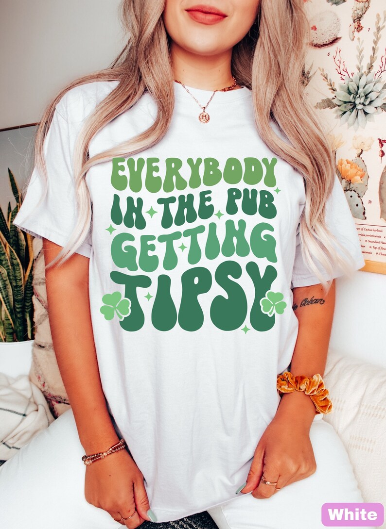 Puede incluir: Camiseta blanca con la frase "EVERYBODY IN THE PUB GETTING TIPSY" en verde. El dise&ntilde;o incluye tr&eacute;boles y estrellas. Un estilo casual y c&oacute;modo.