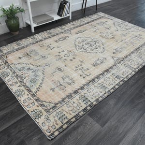 May include: A rectangular area rug featuring a faded beige and cream base with intricate dark grey and charcoal floral and geometric patterns. The design includes a central medallion and a wide, detailed border with repeating motifs.